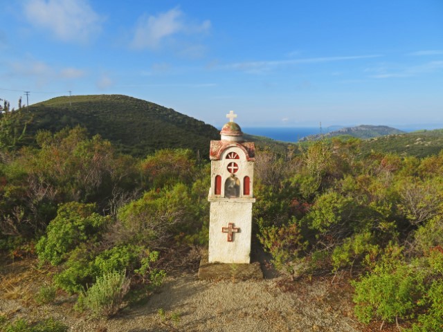 Türmchen mit Kreuz in grünen Hügeln, im Hintergrund das Meer