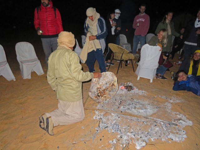 Ein Mann backt am Lagefeuer in der Wüste Fladenbrot