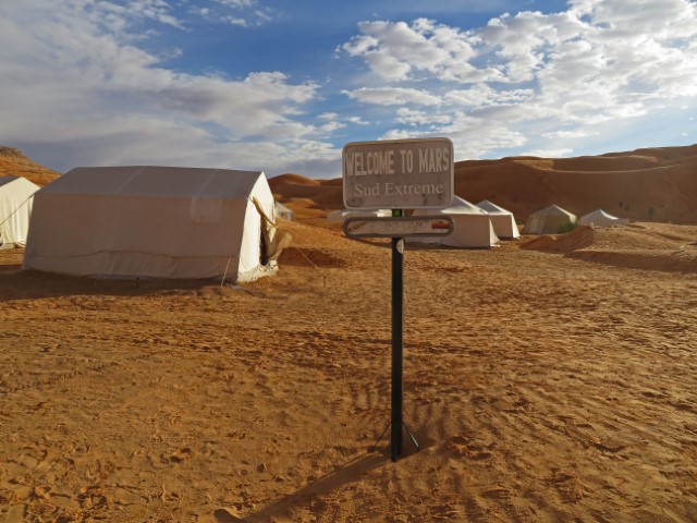 Schild "Welcome to Mars" vor einem Wüstencamp mit weißen Zelten