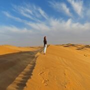 Junge Frau steht im Abendlicht auf einer Düne in der Sahara