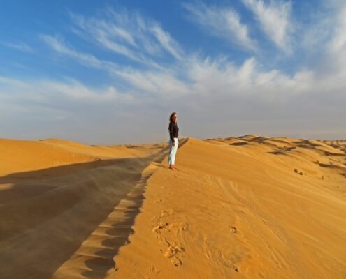 Junge Frau steht im Abendlicht auf einer Düne in der Sahara