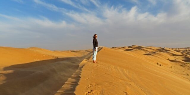 Junge Frau steht im Abendlicht auf einer Düne in der Sahara