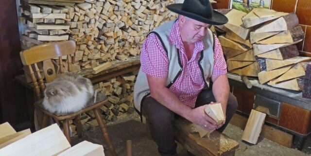 Schindelmacher am Schniedesel, umgeben von Holzscheiten und einem Kater