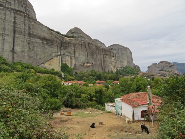 Blick auf ein kleines Haus mit Tieren im Garten, dahinter mächtige Felsen