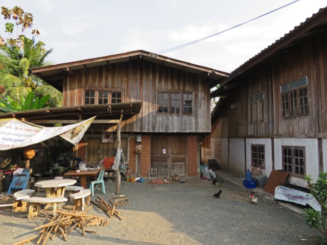 Häuser aus Holz auf dem Land in Thailand, davor ein Hof mit Krempel