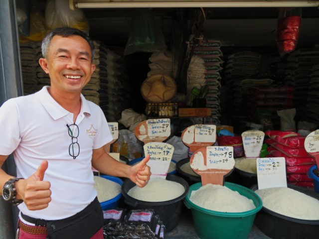 Thai macht das Daumen-hoch-Signal vor einem Stand mit Reis zum Verkaufen