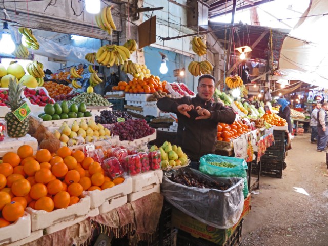 Obstverkäufer vor seinem Stand auf einem Markt in Amman formt mit den Händen ein Herz