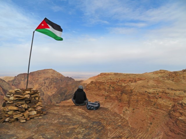 Ein Mann sitzt unter einer jordanischen Flagge und blickt über die Felsenwüste unweit von Petra