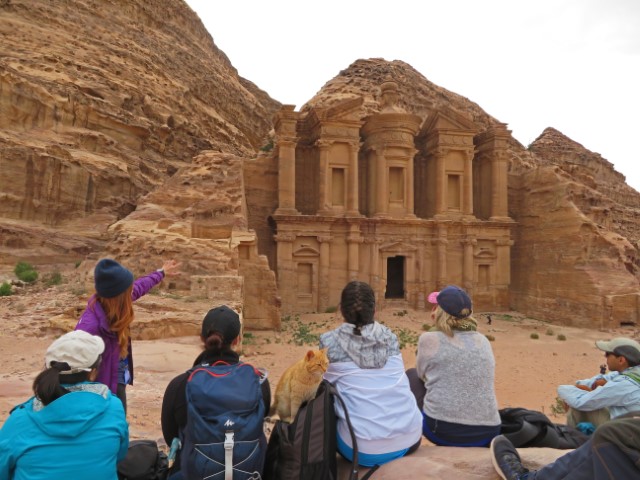 Frauen sitzen mit Blick auf das Kloster Ad Deir in Petra, zwischen ihnen eine rote Katze