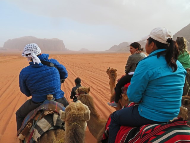 Mehrere Leute sitzen auf Kamelen und reiten auf Wadi Rum zu