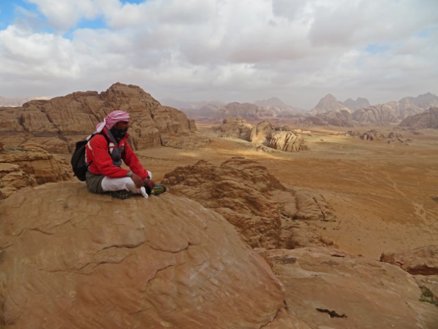 Beduine sitzt auf einem Felsen vor dem Wüstenpanorama Wadi Rums