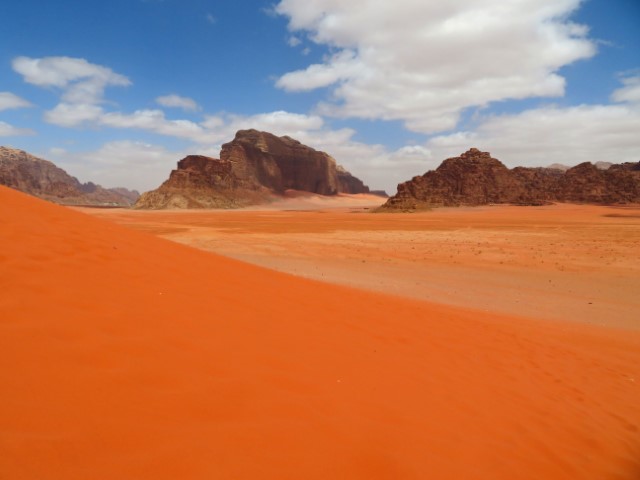 Blick über den knallig roten Sand zu Felsen in Wadi Rum