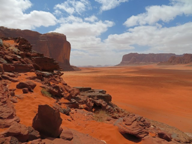 Blick über eine rotsandige Wüstenlandschaft mit hohen Felsen