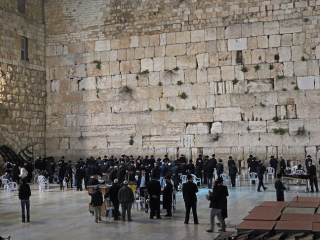 Viele Männer in langen schwarzen Roben stehen nachts an der Klagemauer in Jerusalem.