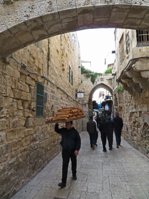 Mann trägt riesen Tablett mit Baguettes auf dem Kopf durch eine dunkle Gasse von Jerusalem