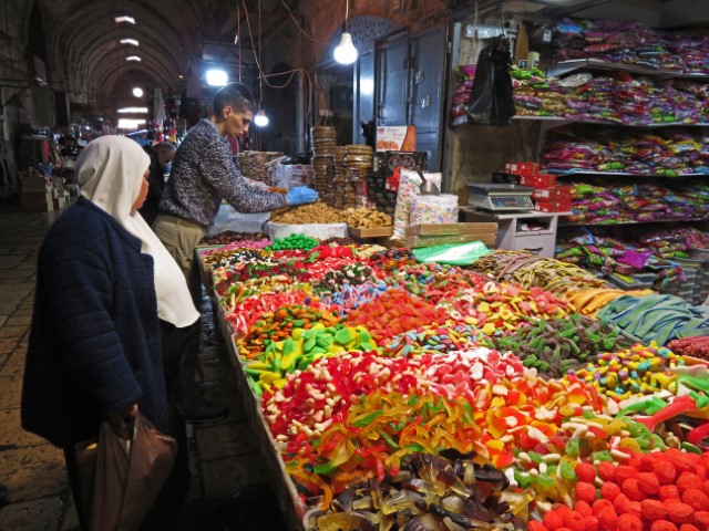 Riesiger Stand mit Süßigkeiten auf einem Markt in Jerusalem, die sich eine Frau mit Kopftuch anschaut