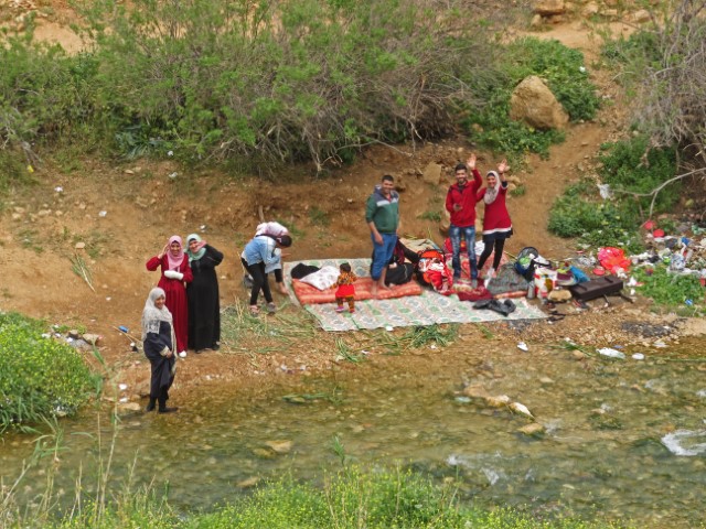 Palästinensische Familie macht an einem Fluss Picknick und winkt