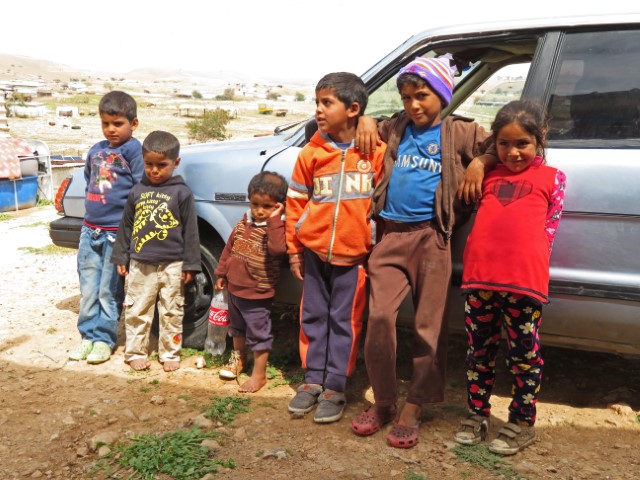 Kinder in abgerissener Kleidung in der Al-’Auja Gemeinde lehnen an einem alten Auto