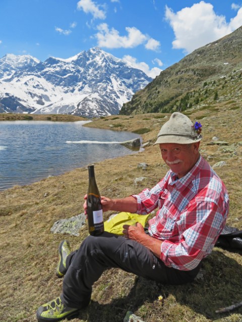 Wanderführer an einem Bergsee mit Weinflasche in der Hand