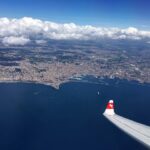 Flugzeug der Swiss Air fliegt über Wasser, im Hintergrund sieht man Land