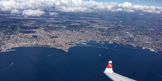 Flugzeug der Swiss Air fliegt über Wasser, im Hintergrund sieht man Land