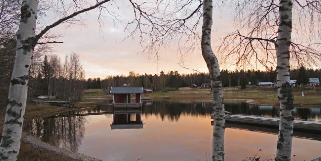 Rotes Häuschen in Schweden spiegelt sich bei Sonnenuntergang auf See